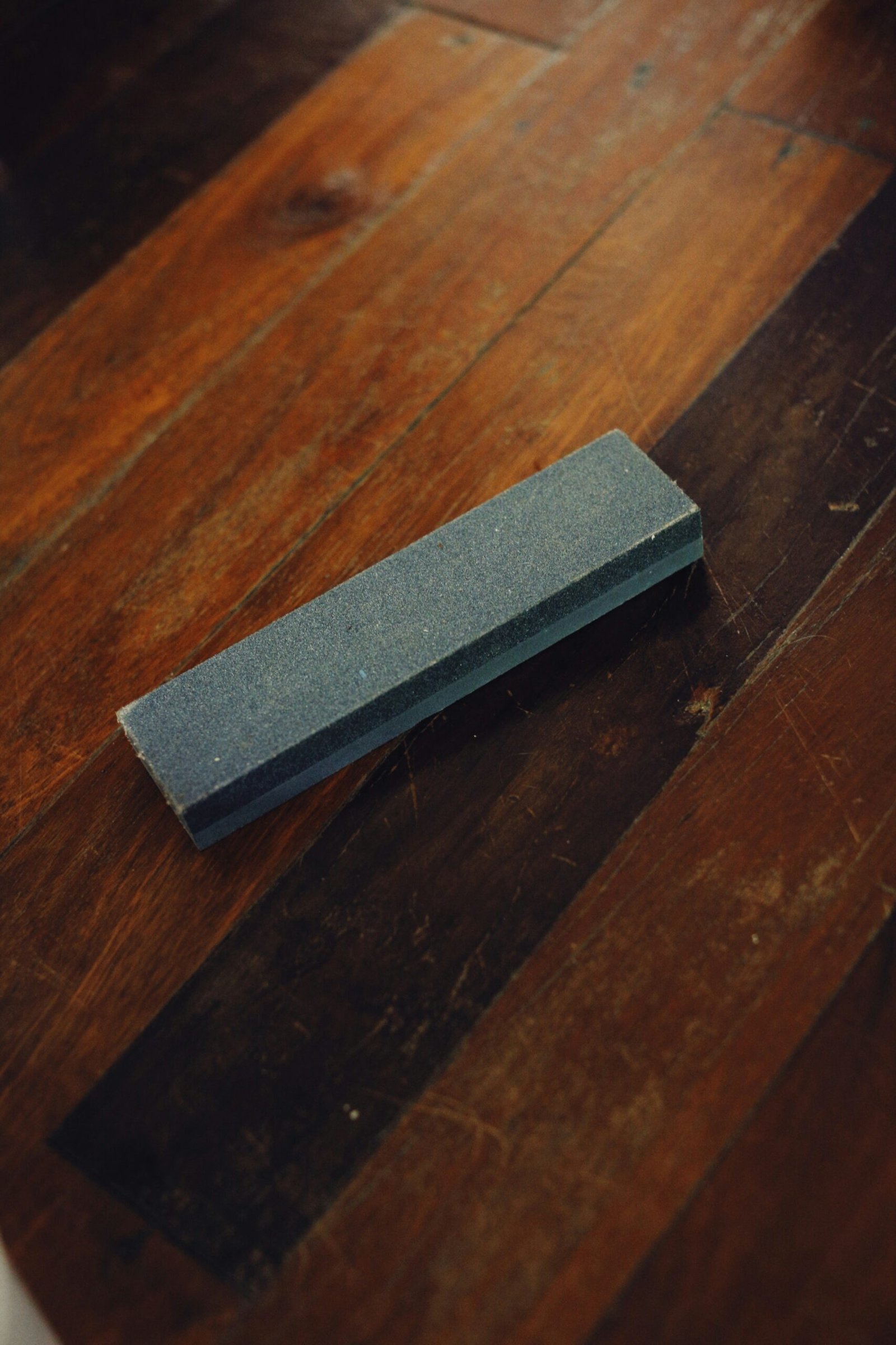 A rectangular sharpening stone resting on a dark wooden surface.